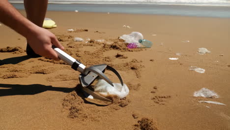 volunteer uses a litter picker to clean up plastic trash on a polluted beach