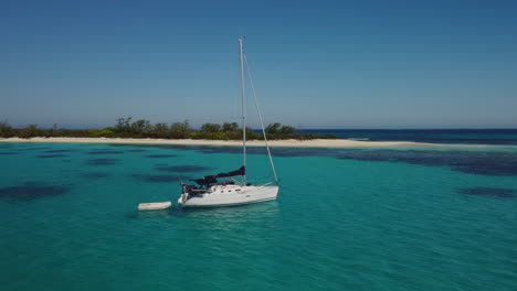 low close aerial parallax around sailboat anchored near small island, isle of pines