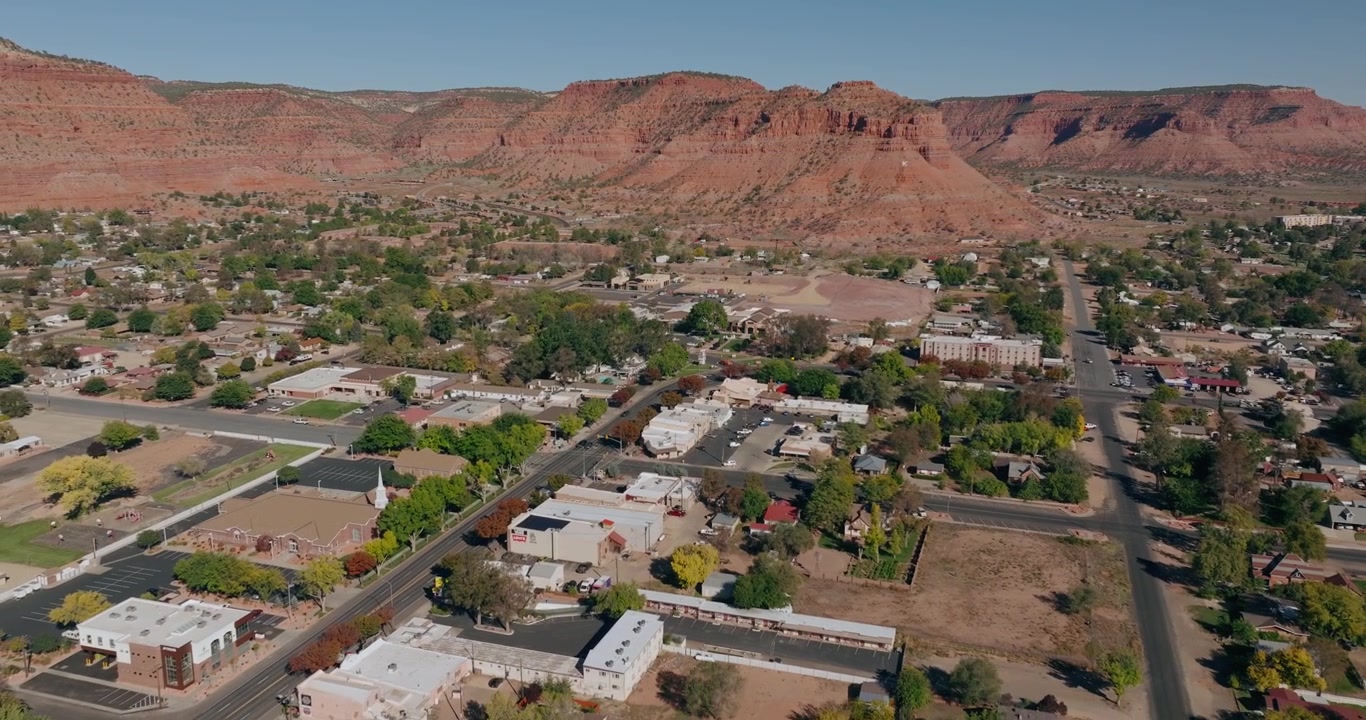 Ripresa aerea in allontanamento delle strade, case ed edifici della città di Kanab, Utah, sotto imponenti scogliere di arenaria rossa, con drone