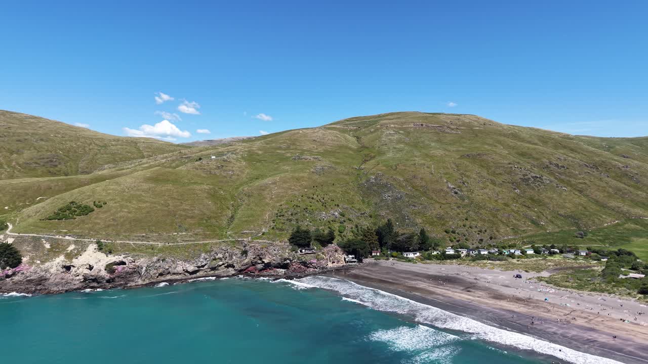 Flying above beautiful turquoise sea on a sunny day with volcanic rock and walkway in distance (Taylors Mistake Beach, Canterbury, New Zealand)