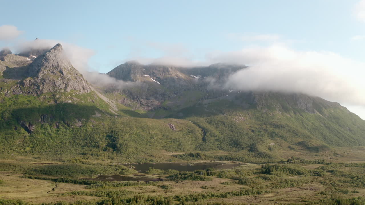Slow aerial shot capturing lush forested mountains and drifting clouds in soft morning light.