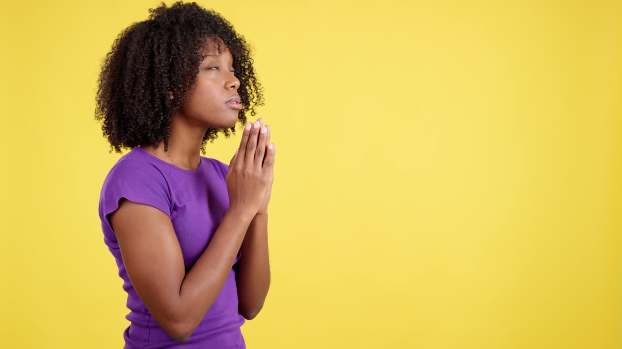 Woman Praying with Hands Clasped Against Yellow Background