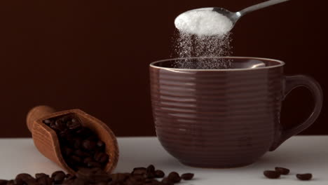 sugar pouring into brown coffee cup