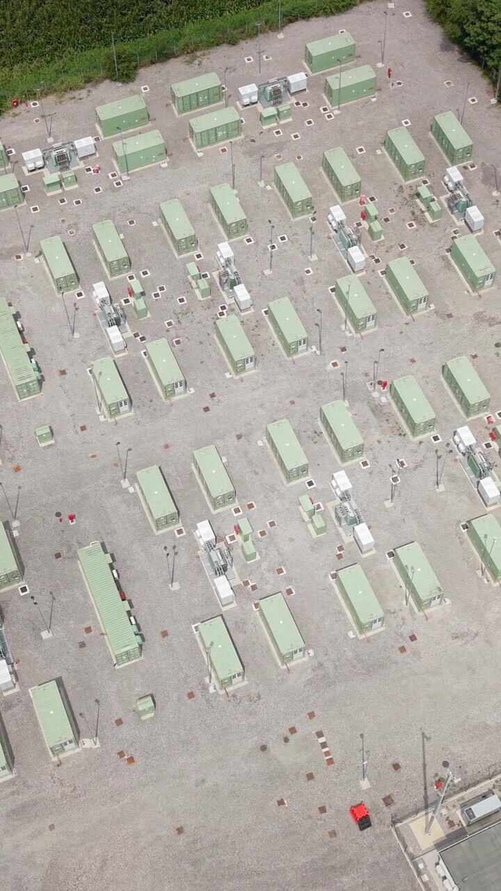 Vista aerea di un impianto di accumulo di batterie su scala industriale accanto a sottostazioni elettriche e linee di trasmissione, che illustra la tecnologia di accumulo dell'energia e la modernizzazione della rete elettrica italiana