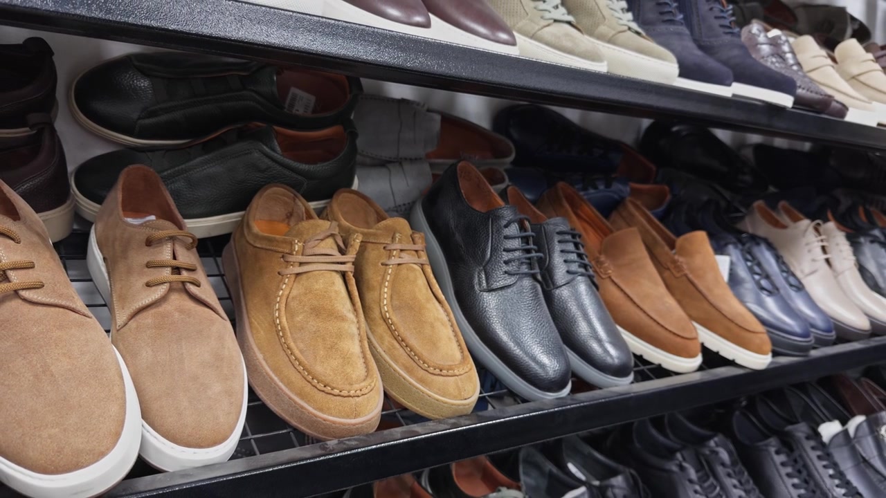 Hochwertige 4K-Nahaufnahme von Premium-Herren-Ledersneakern und klassischen Schuhen in einem Ladenregal. Präsentiert elegantes Schuhdesign, Handwerkskunst und eine Modekollektion für den Einzelhandel.