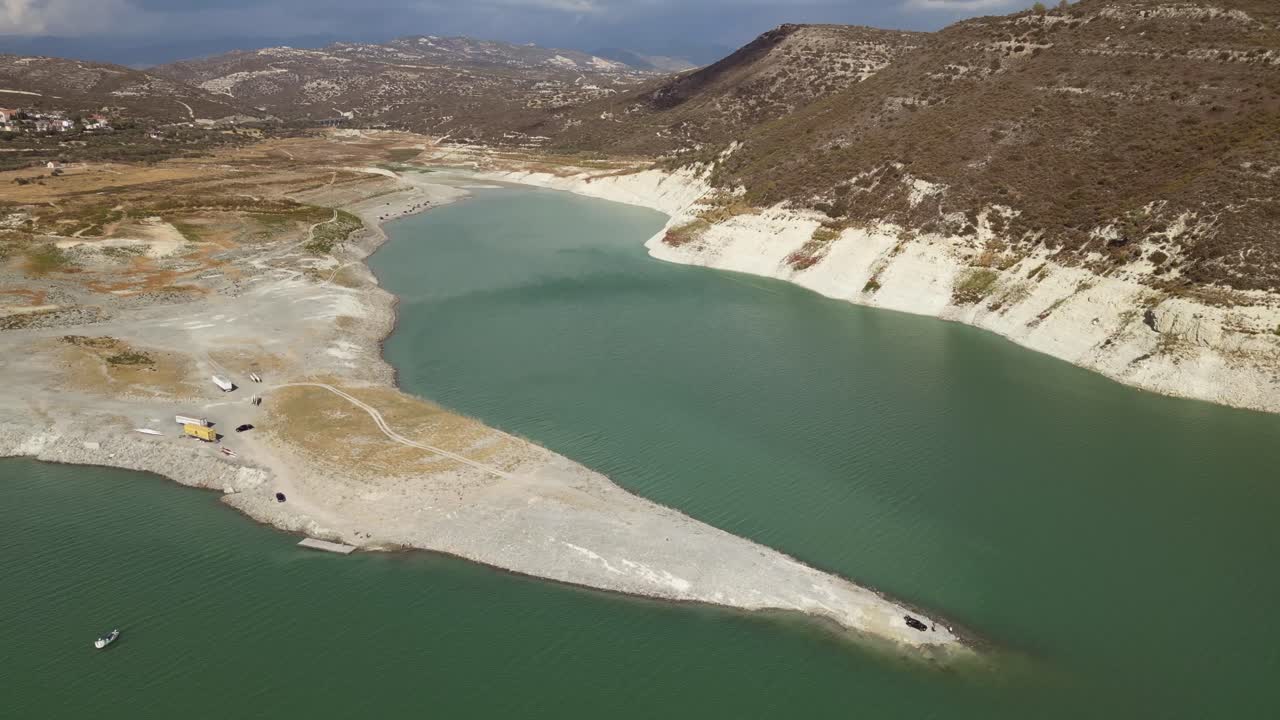 An aerial cinematic drone shot showcases the expansive Kouris Dam, highlighting its tranquil waters, surrounding rugged terrain, and the breathtaking harmony of nature and engineering.