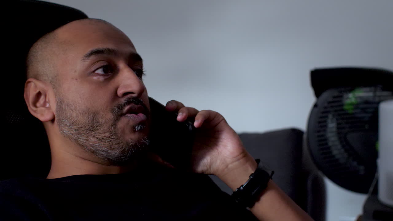A man is casually seated on a rolling chair, chatting on his mobile phone, embodying the idea of a relaxed domestic lifestyle