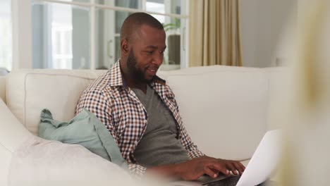 hombre afroamericano usando una computadora portátil mientras está sentado en el sofá en casa