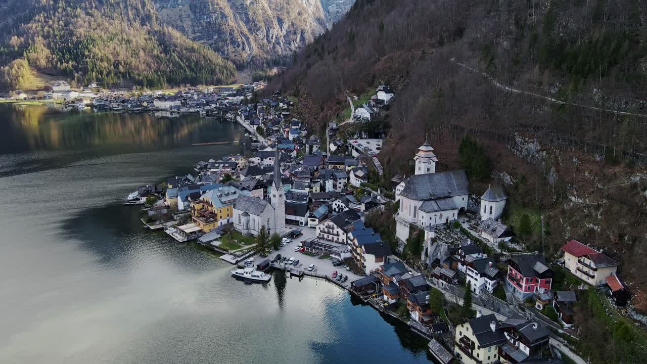 Golden light reflects off alpine lake, quaint town sits beneath forested slopes