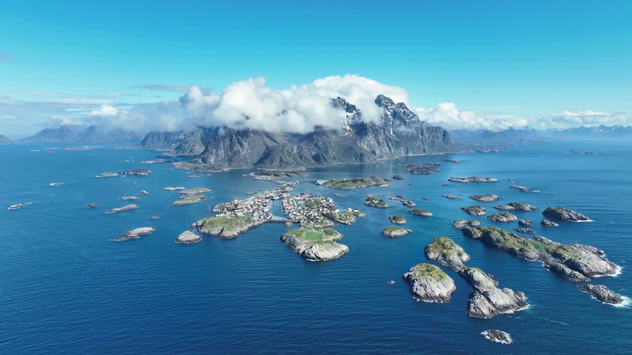 Very high wide aerial over Henningsvaer showing islands, sea horizon and dramatic mountains