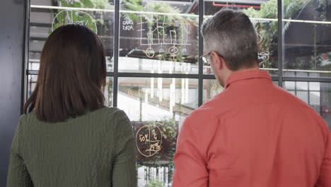 rear view diverse male and female colleague brainstorming on glass wall in office, slow motion