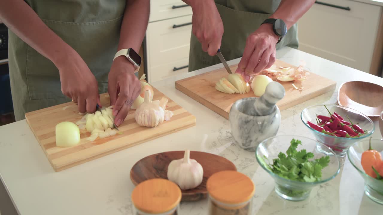 Couple in green aprons after peeling onions, chopping and dicing on adjacent boards, preparing meal