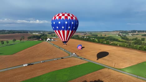 aerial view of flying hot air balloon with american flag and stars above rural american area an driving cars on road