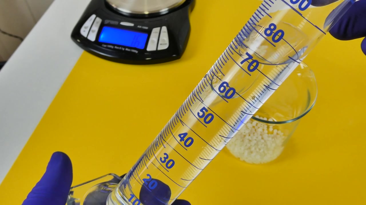 Técnico de laboratório despejando um líquido transparente de uma proveta em um béquer de vidro