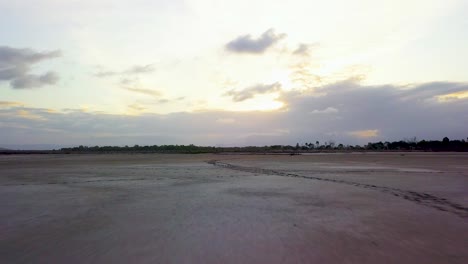 drone flying low, fast and straight over winding animal tracks on large mud flats and then rising to reveal beautiful cloudy sunset