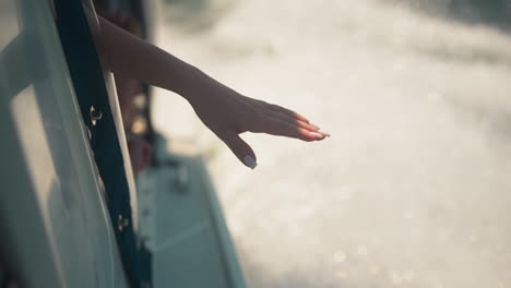 passenger holds hand out of yacht window touching water sprays on holiday trip closeup. woman enjoys freshness sailing sea on summer vacation