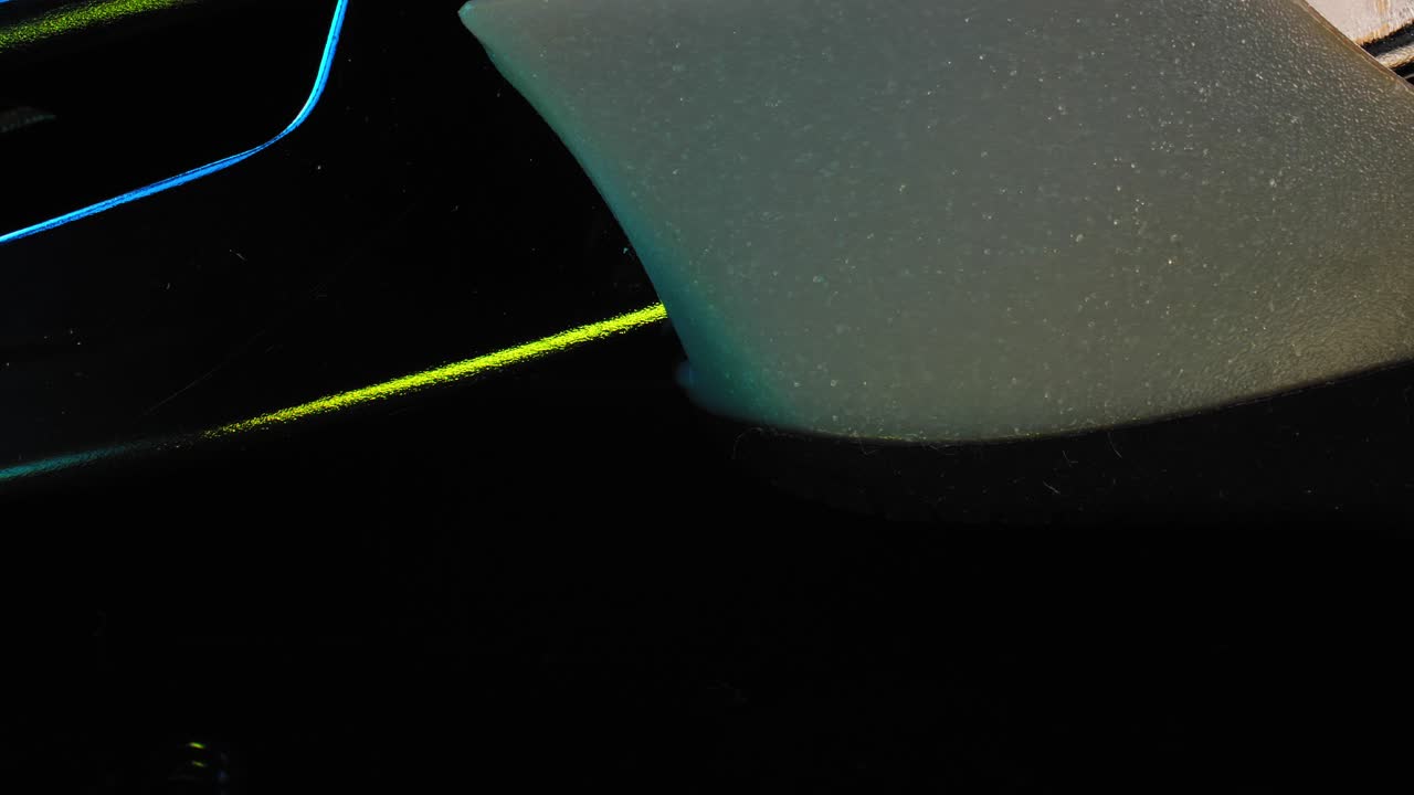 A close up of the handle of a stapler with a black background slowly panning the sleek and illuminated outlines in brilliant blue and green lights