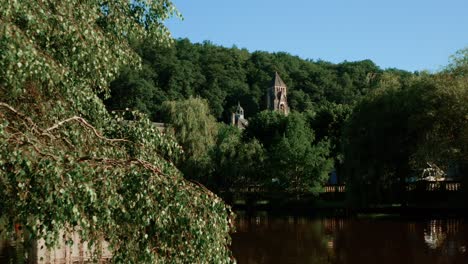 Brantôme-town-hall,-drone-view-behind-trees,-ground-level-view-of-river