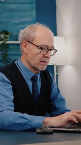 vertical video: focused old entrepreneur checking graphics writing on laptop
