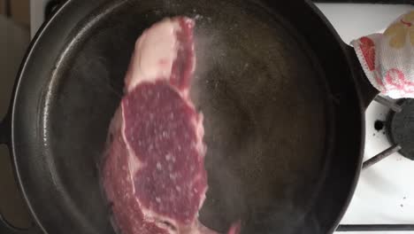 placing a raw steak into a hot cast iron skillet with oil - overhead view