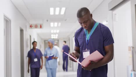 video portrait of african american male doctor with folder smiling in hospital corridor, copy space