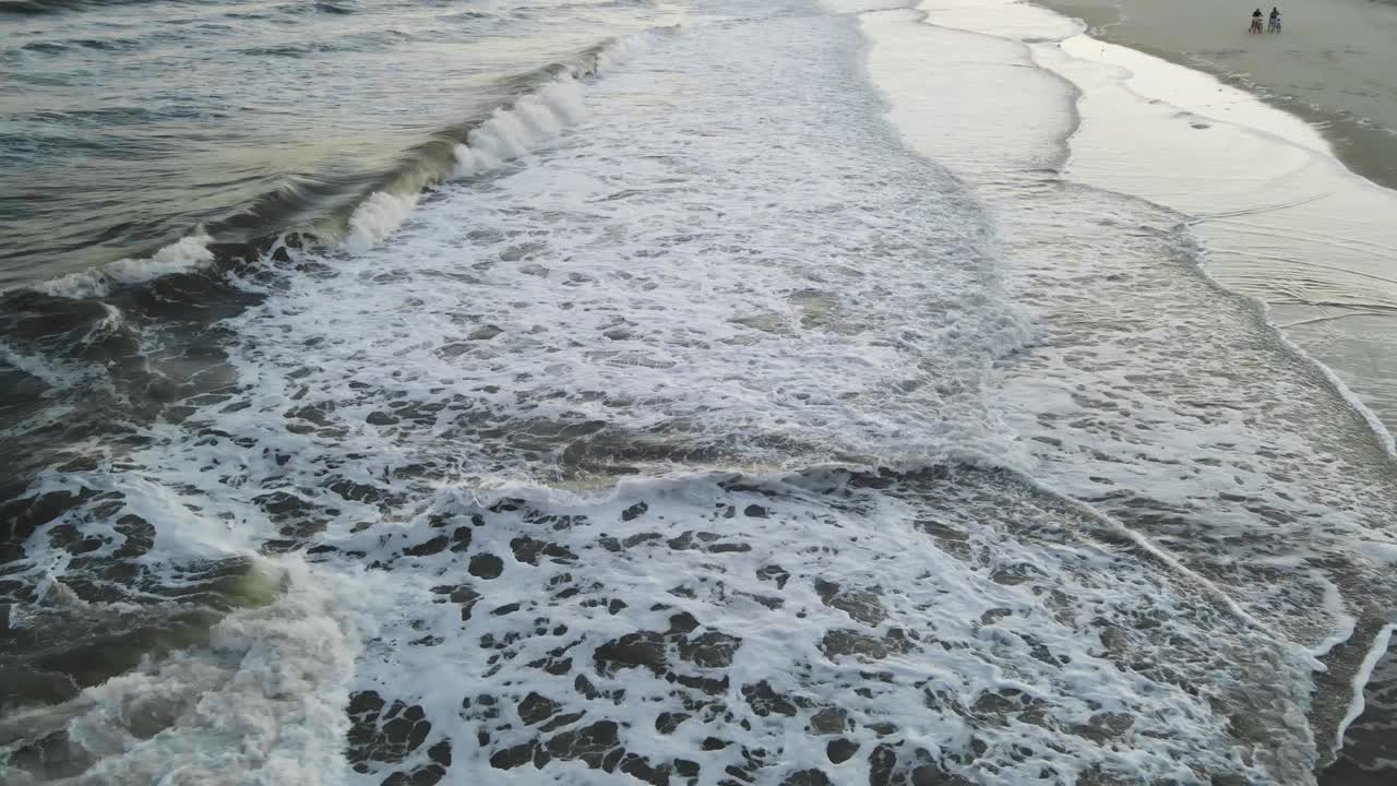 Wide drone shot flying down on beach with distant bicyclist