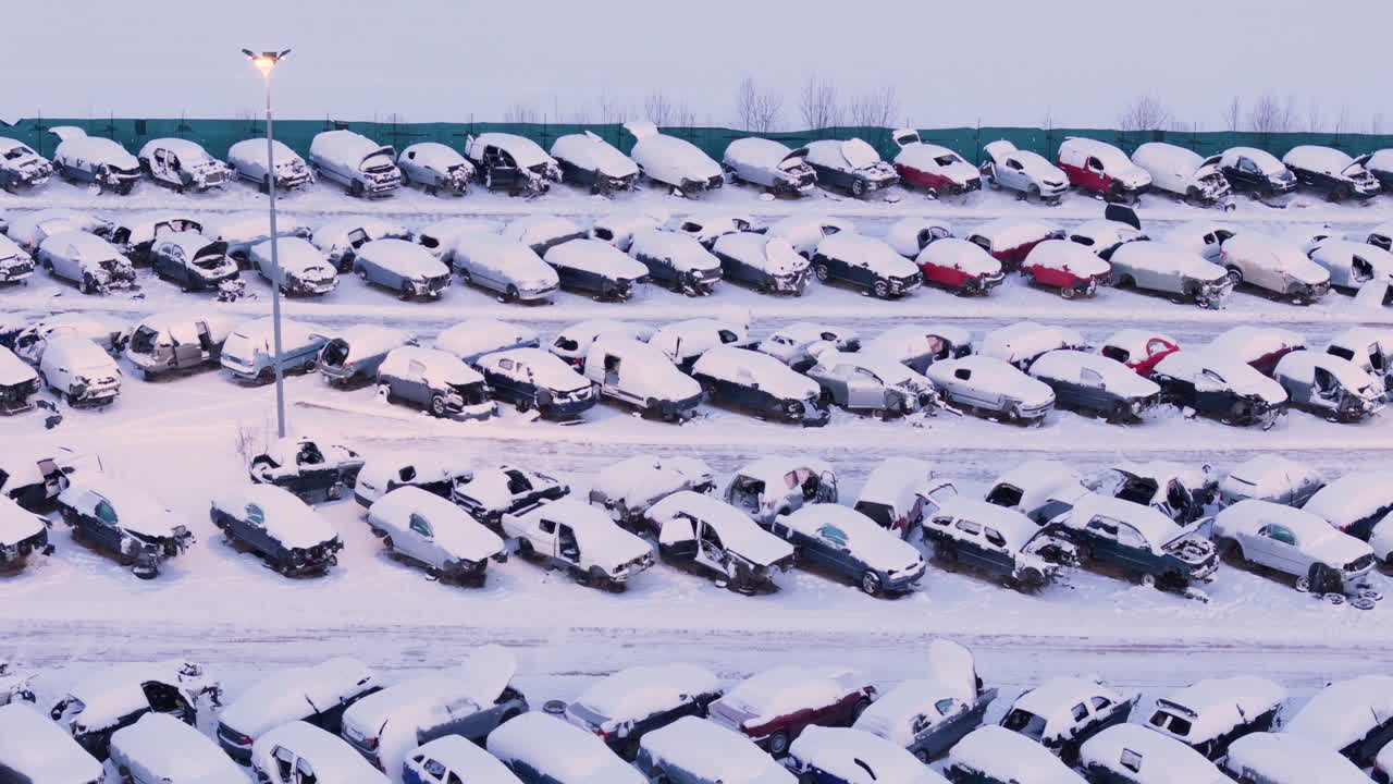 Broken down wrecked vehicles at scrap yard covered in winter snow, aerial view