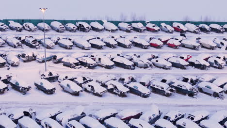broken down wrecked vehicles at scrap yard covered in winter snow, aerial view