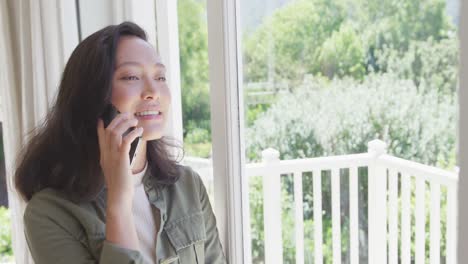 happy asian woman talking on smartphone and looking through window, in slow motion