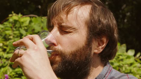 slow motion footage of young bearded man drinking glass of water to quench thirst during heatwave