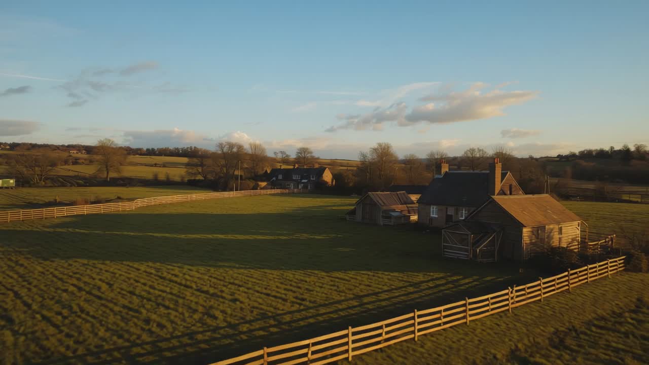 Drone initiating forward descent over rural grassy pasture, revealing barn cluster and barn doors