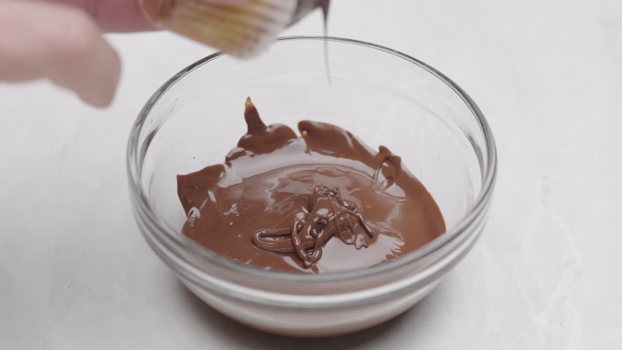 Mano che intinge un muffin nel cioccolato fuso in una ciotola di vetro, primo piano della preparazione del dolce