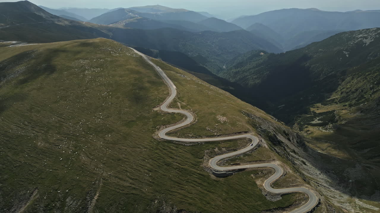 Breathtaking aerial view of Romania's Transalpina road, weaving through majestic green mountains under a clouded sky