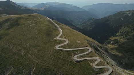 Impresionante-Vista-Aérea-De-La-Carretera-Transalpina-De-Rumania,-Serpenteando-A-Través-De-Majestuosas-Montañas-Verdes-Bajo-Un-Cielo-Nublado