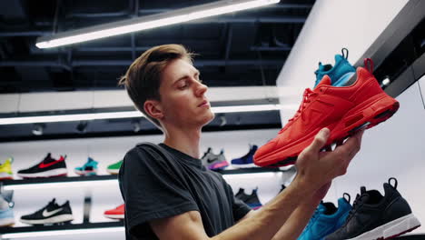 a young man examines a pair of red sneakers in a shoe store