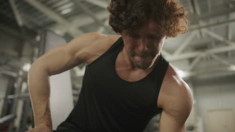 muscular athlete doing seated one-arm dumbbell curls in gym