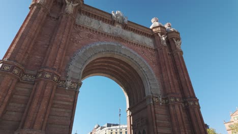 the majestic arc de triomf stands under a clear blue sky in barcelona, showcasing its detailed red brick architecture. pan left shot