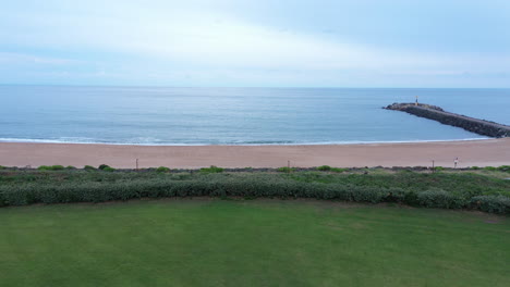 Toma-Aérea-De-Hierba-Verde-Frente-A-Una-Playa-De-Arena-Aguas-Tranquilas-Océano-Atlántico