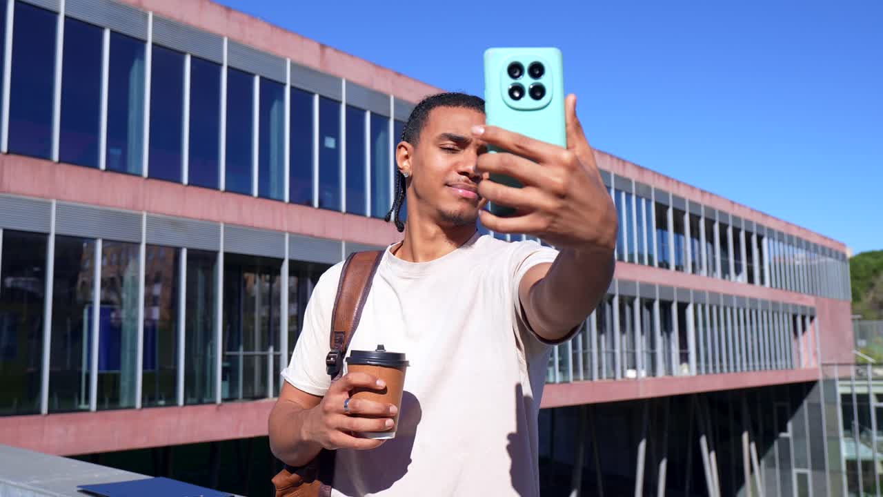Giovane uomo che fa un selfie con una tazza di caffè nel campus universitario.
