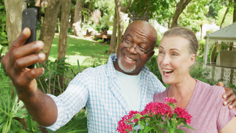 happy senior diverse couple wearing shirts and taking selfie with smartphone in garden