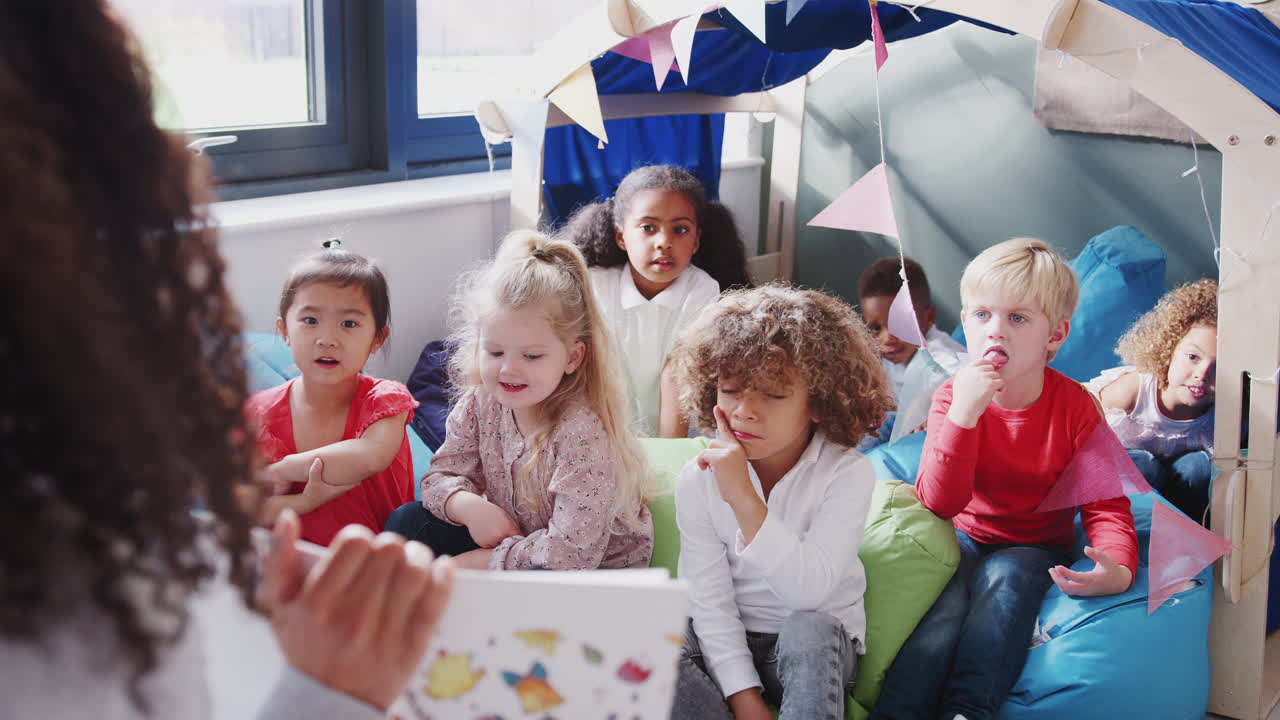 vista por encima del hombro del maestro mostrando el libro a los niños sentados en una esquina cómoda del aula