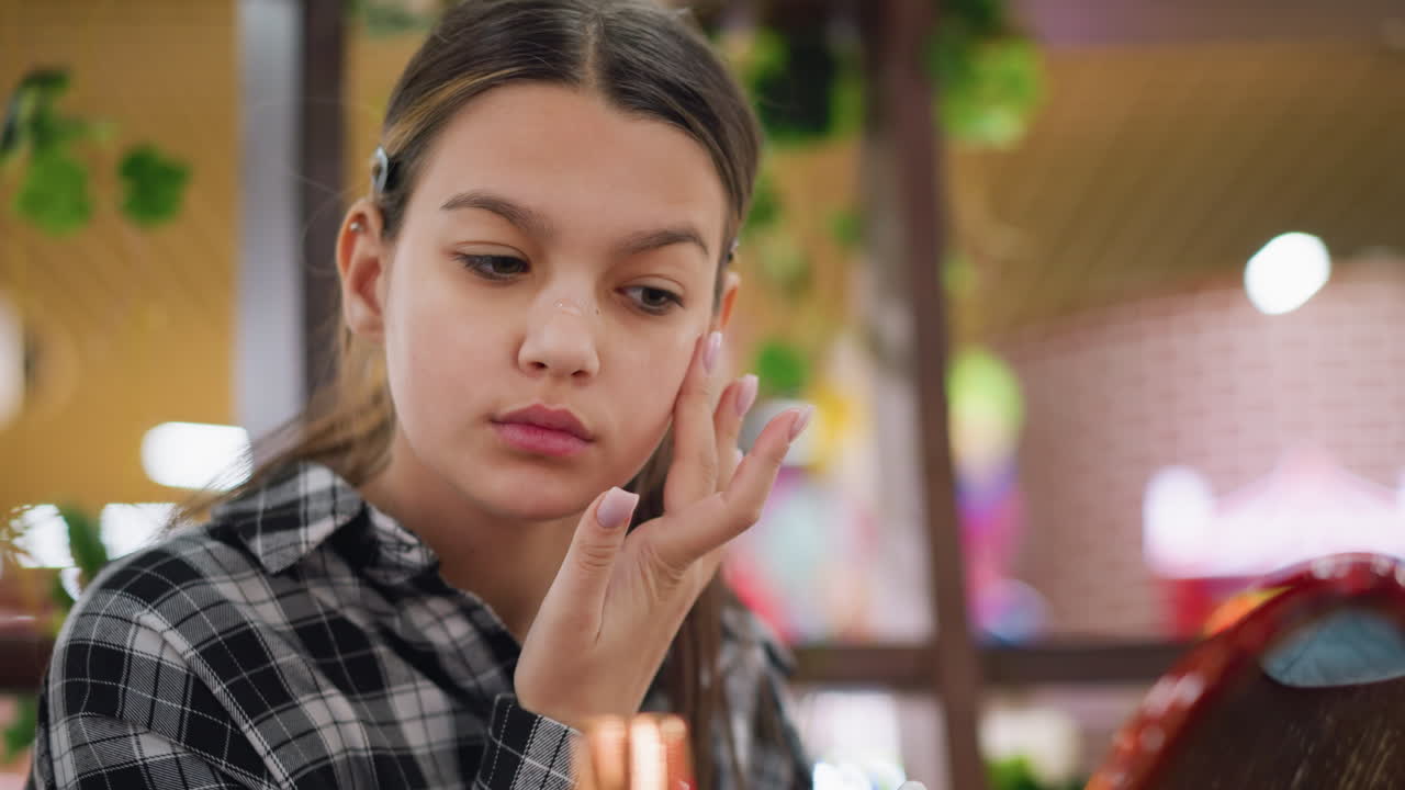 젊은 소녀가 거울을 보면서 얼굴에 세럼 메이크업을 적용하는 클로즈업, 집중된 표정은 빛나는 피부, 부드럽고 자연스러운 아름다움 증진을위한 아름다움 루틴과 수분을 강조합니다.