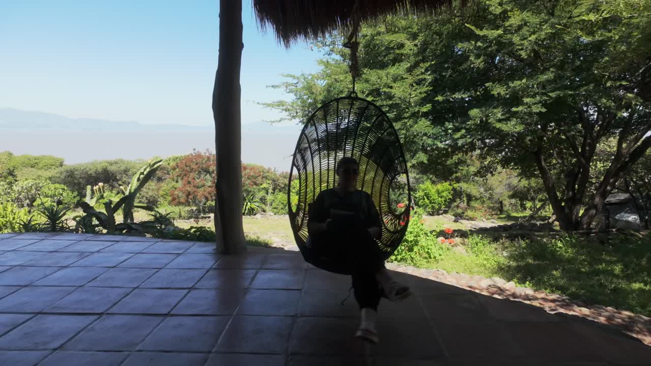 Serene shot of a woman in swinging in a hanging egg chair, taking in mountain views and enjoying a quiet retreat with scenic greenery