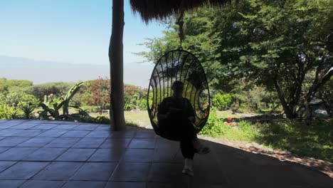 serene shot of a woman in swinging in a hanging egg chair, taking in mountain views and enjoying a quiet retreat with scenic greenery