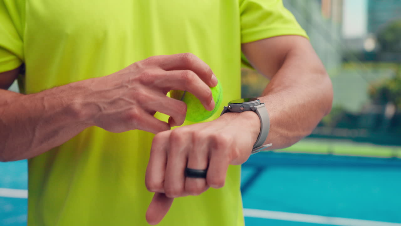 Atleta che controlla lo smartwatch mentre tiene una pallina da tennis in campo