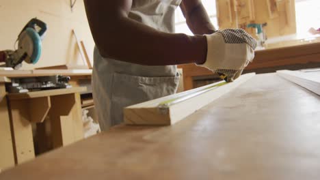 African-american-male-carpenter-measuring-and-making-pencil-markings-on-wooden-plank