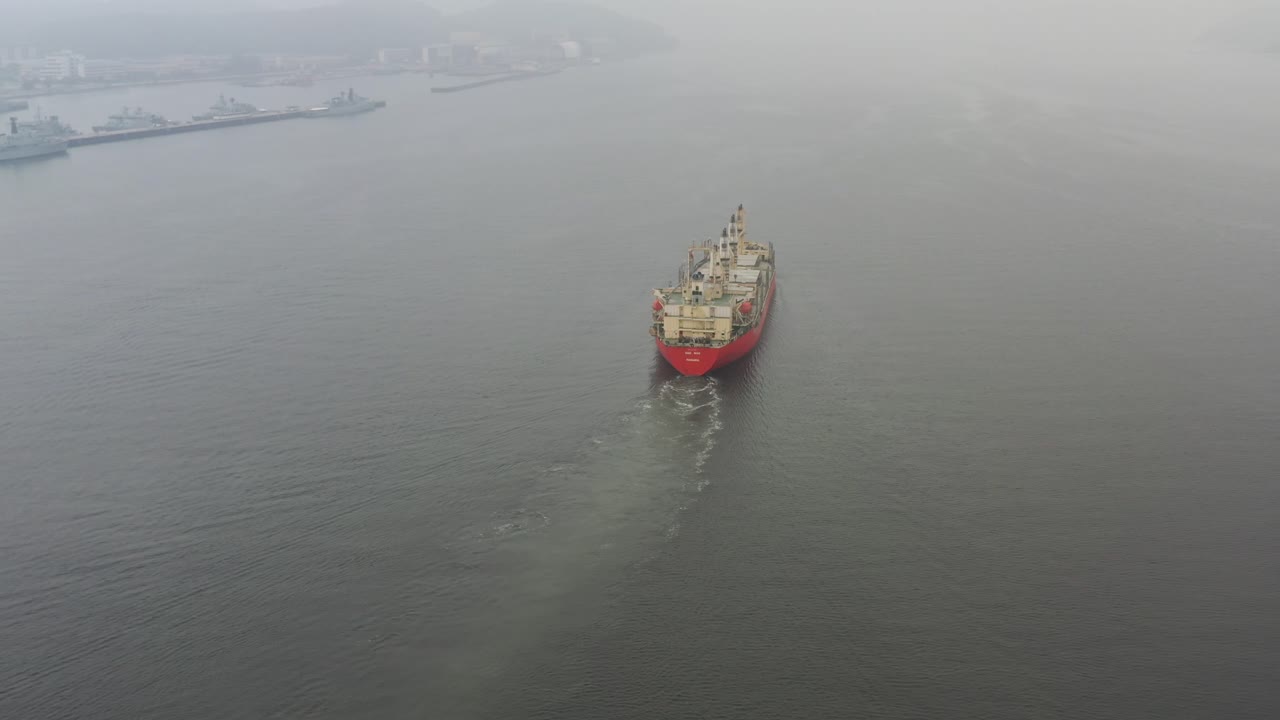 Large international cargo ship, empty barge with no shipments sailing slowly on the sea into the wilderness on a foggy morning at Lumut, Manjung, Perak, Malaysia, southeast asia, aerial drone shot.
