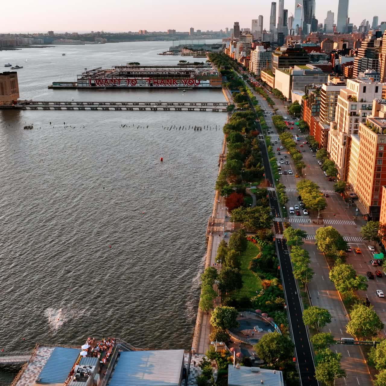 Flight above the waterfront of Hudson River. Beautiful green park and highway separating water from buildings. Aerial perspective
