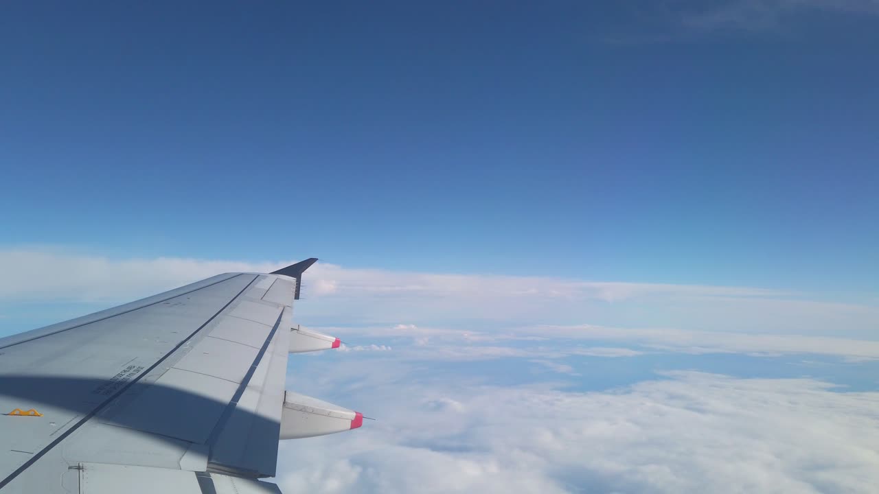 Ala di aereo in volo sopra le nuvole con cielo blu.