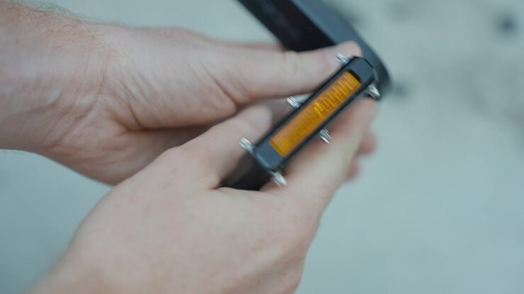 Hands inspecting a gravel bike pedal with reflector and metal pins.